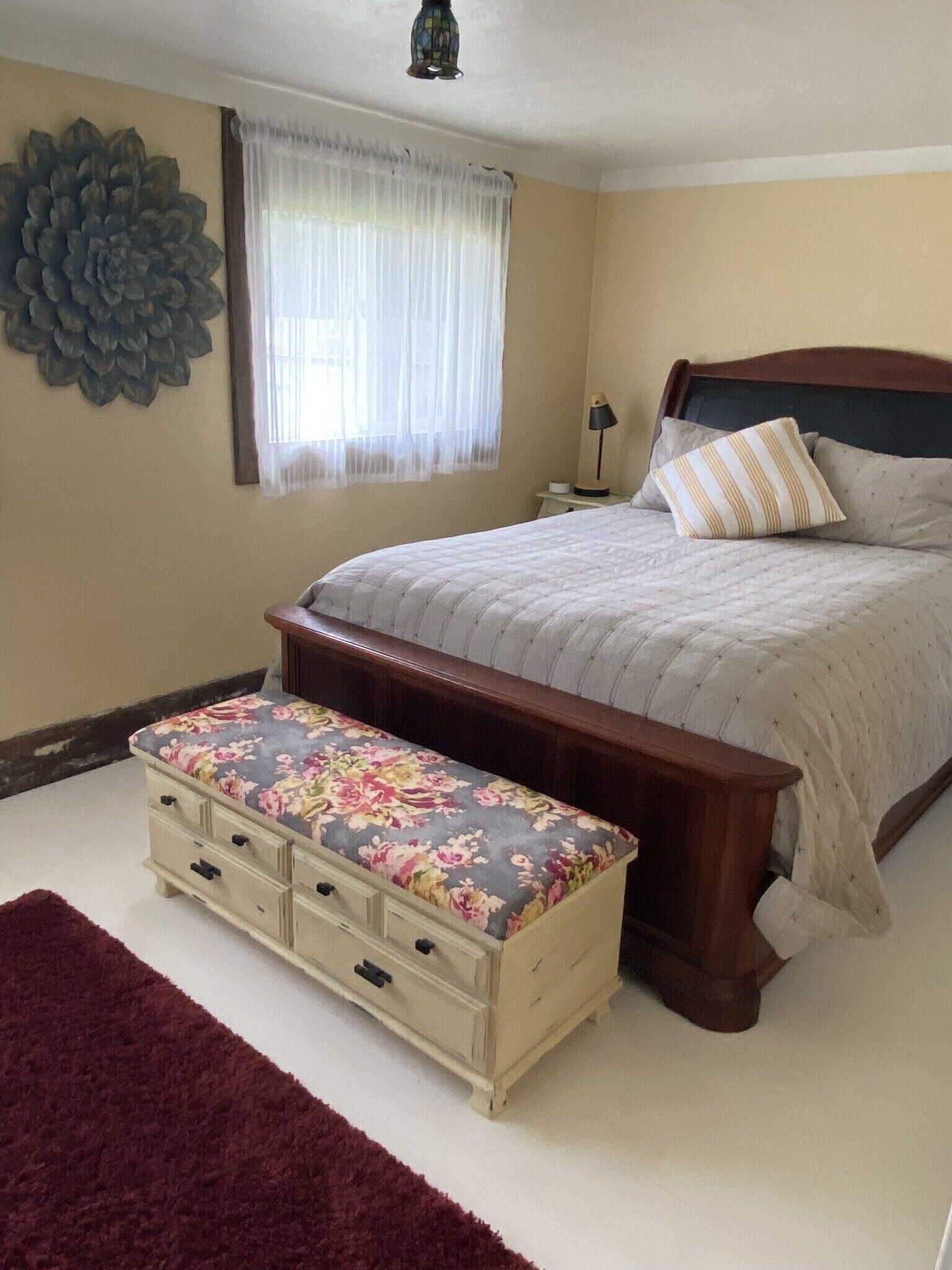 Ein Schlafzimmer mit Bett, Nachttisch, Lampe, einer Blumenbank und einem großen Wanddekor.