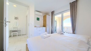 A hotel room with a large bed, a desk with a mirror, a vanity, and a balcony with a view.