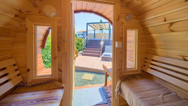 A wooden cabin with a loft bedroom, a balcony, and a view of a house and greenery outside.