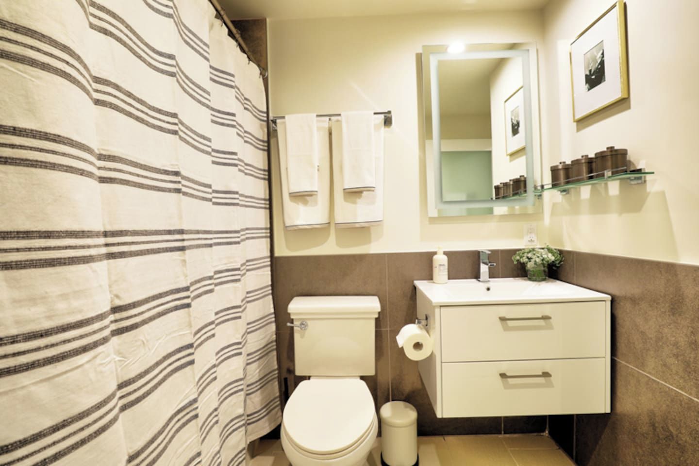 Ein Badezimmer mit gestreifter Duschvorhang, Toilette, Waschbecken mit Spiegel und Ablage für Toilettenartikel.