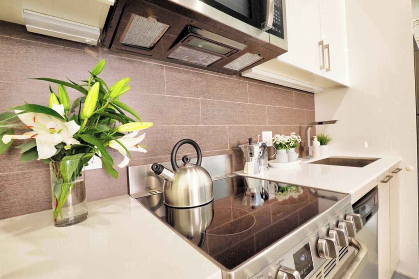 A modern kitchen with a stainless steel kettle, a coffee maker, and a vase with flowers on the counter.