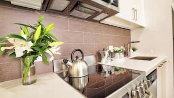 A modern kitchen with a stainless steel kettle, a coffee maker, and a vase with flowers on the counter.