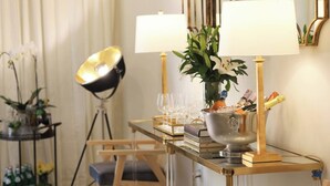 Ein helles Zimmer mit modernem Design, ausgestattet mit einem langen Tisch, einem Champagnerkühler, zwei Lampen und einer Vase mit Blumen.