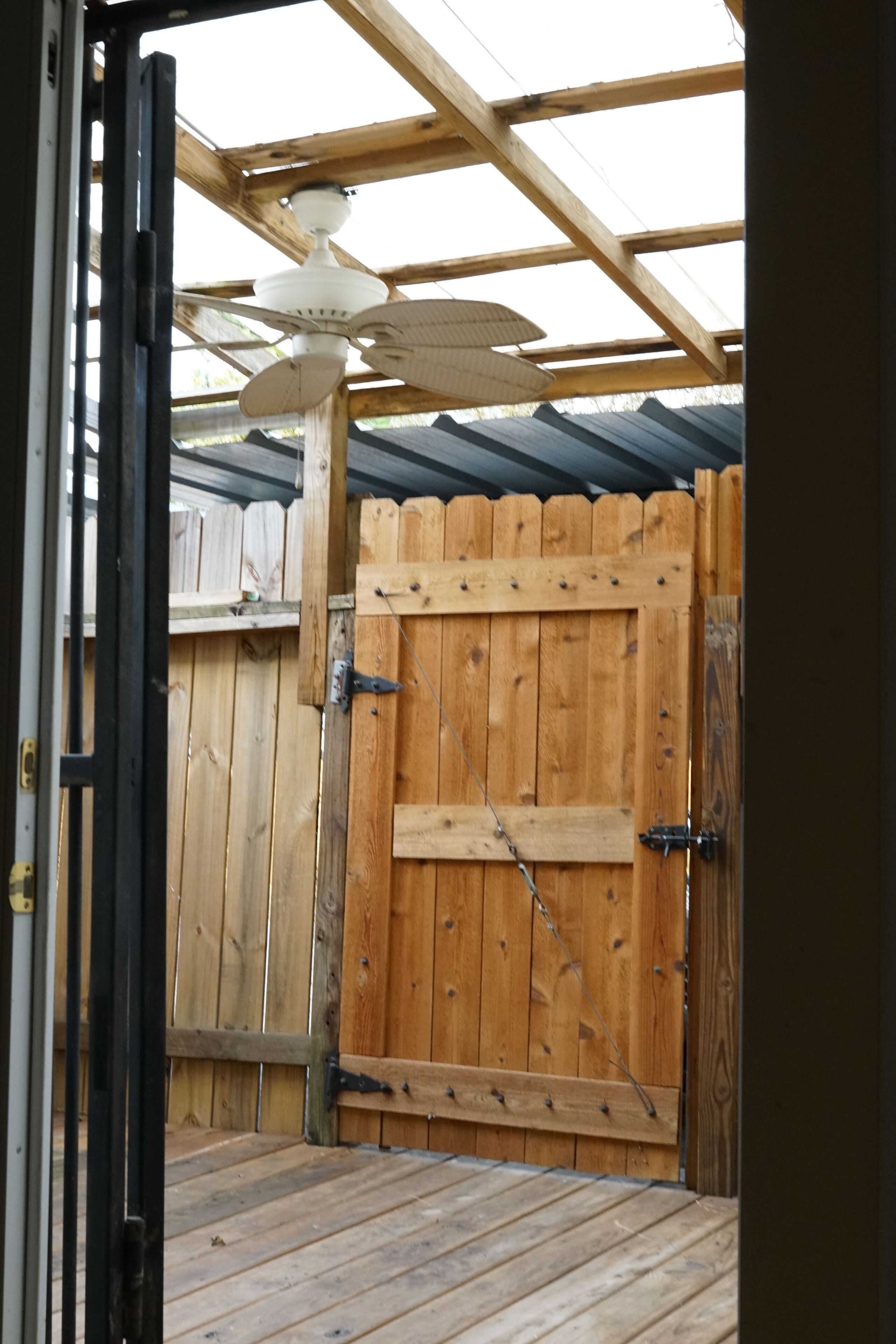 Una puerta de madera con un cierre metálico, una terraza de madera y un ventilador de techo.