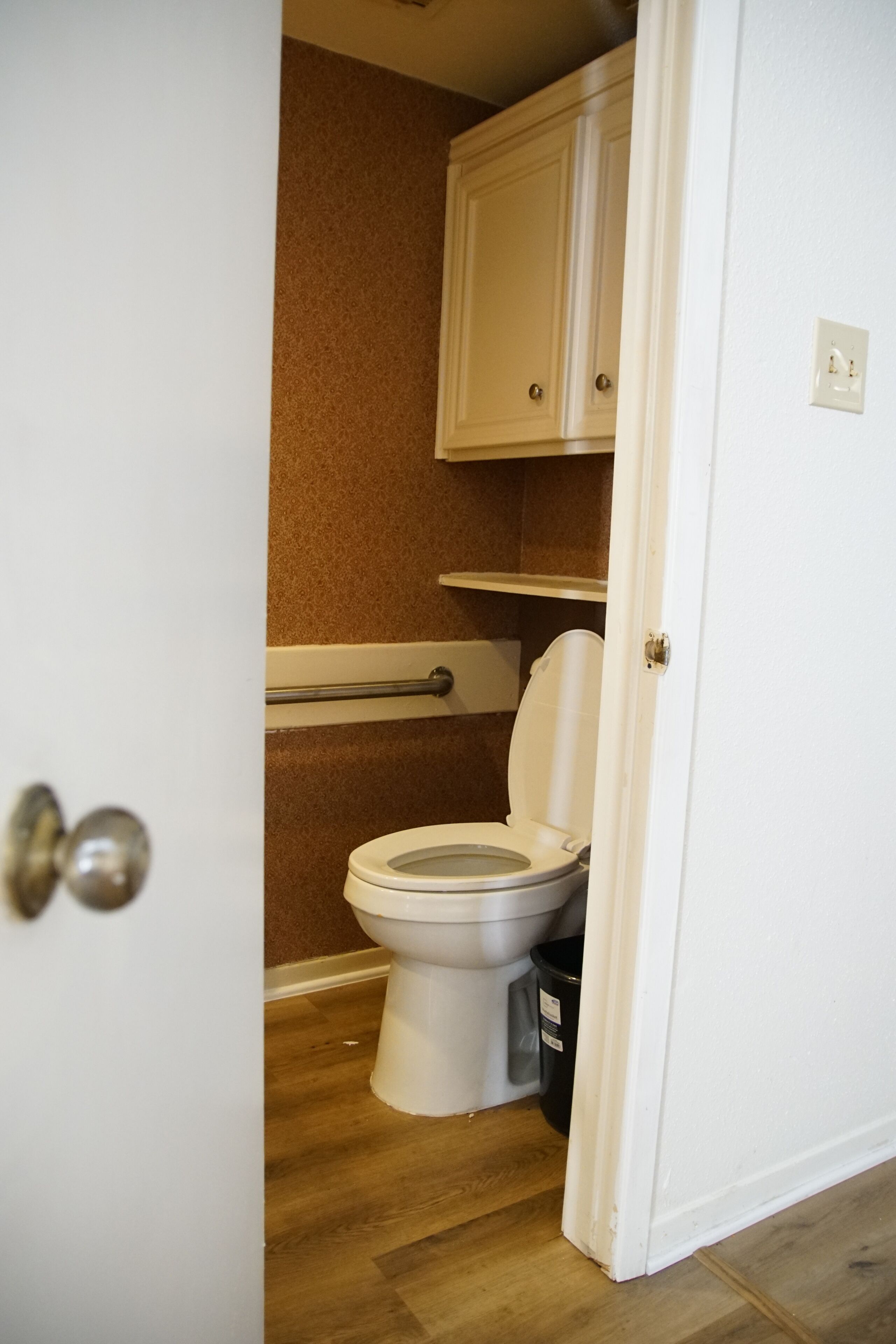 A bathroom with a toilet, a cabinet above it, and a trash bin.