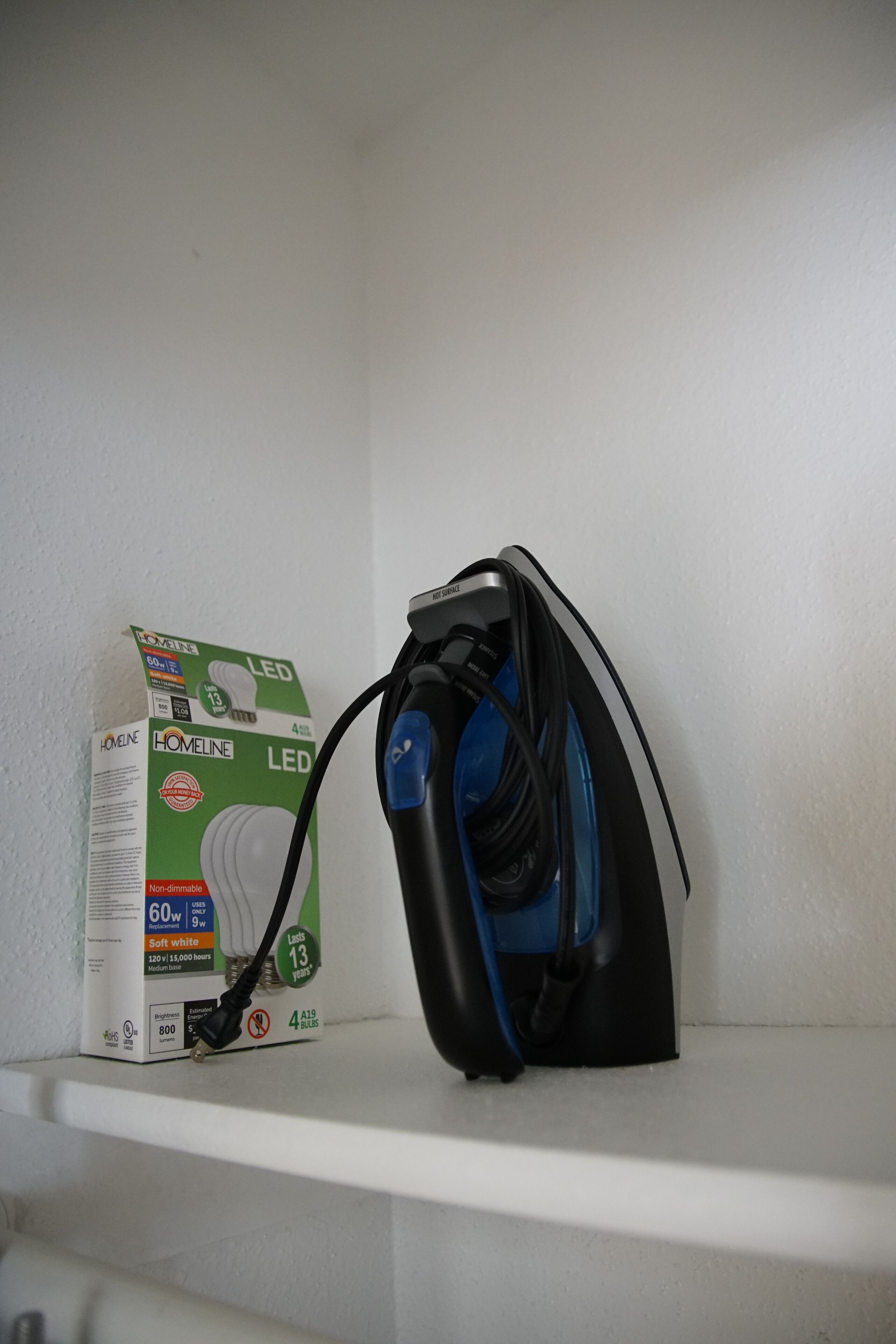 A white shelf with a blue and black iron and a box of LED bulbs.