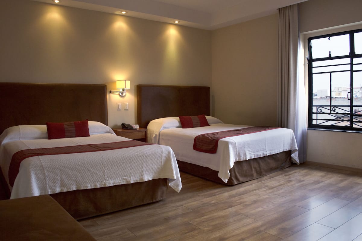 Habitación de hotel con dos camas, piso de madera, una mesita de noche y ventana con vistas.