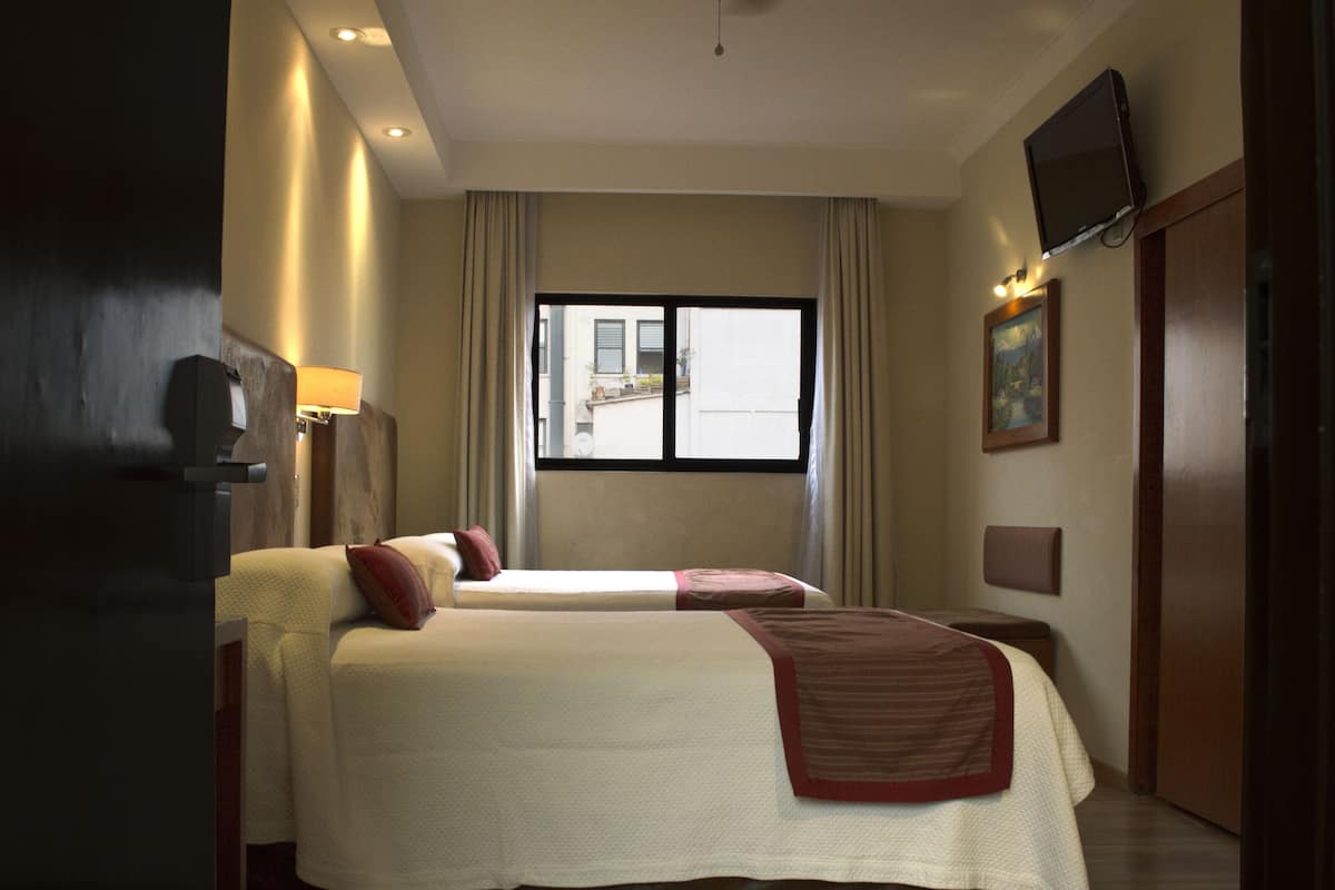 Habitación de hotel con dos camas, televisión, ventana con cortinas y puerta.