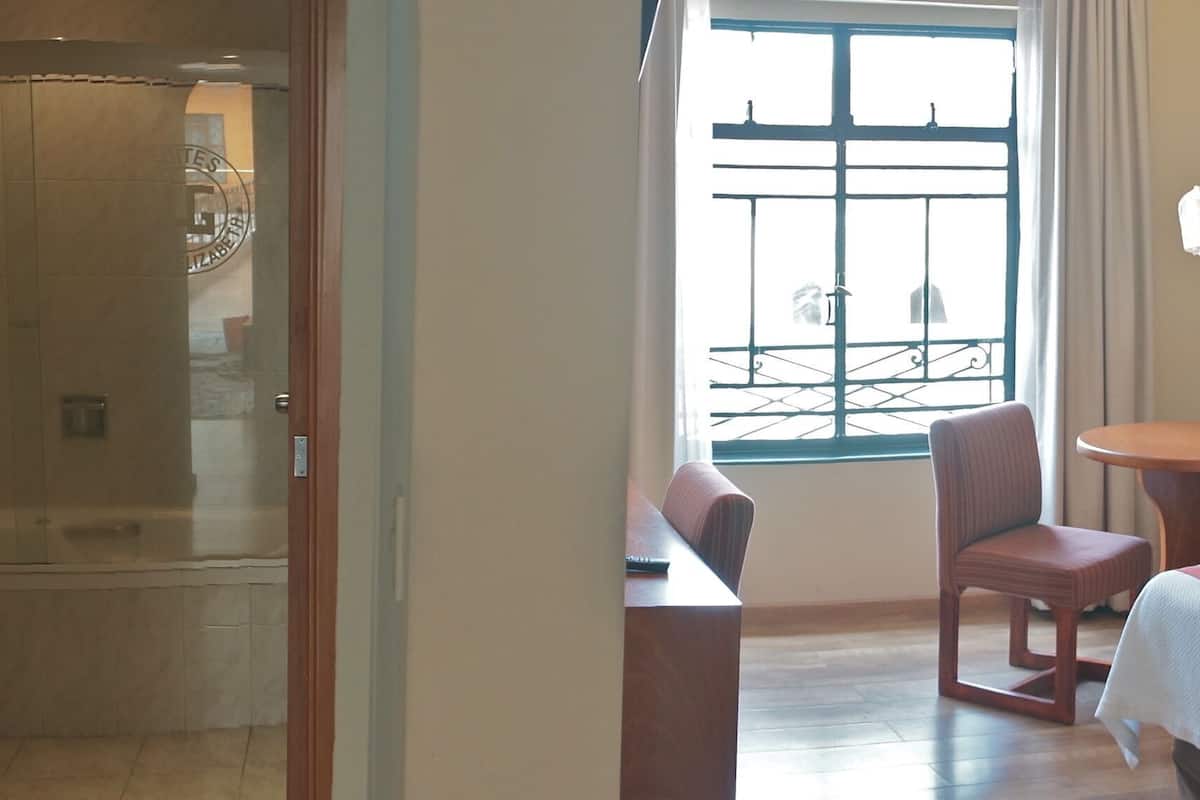 Habitación de hotel con cama, una silla, una mesita, una mesita de noche, una lámpara y vistas al exterior.