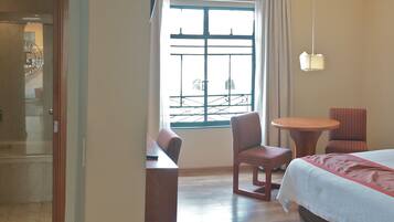 Habitación de hotel con cama, una silla, una mesita, una mesita de noche y ventana con vistas.