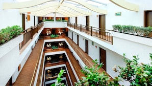 A multi-level atrium with a glass ceiling, wooden flooring, and indoor plants. - Hotel Gillow (Mexico City)