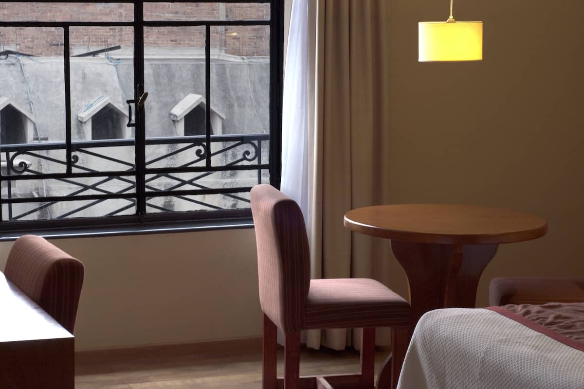 Habitación con vistas a edificios a través de una ventana con reja de metal, una mesa redonda de madera y dos sillas.