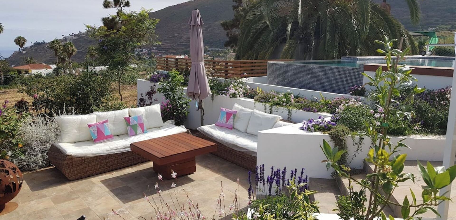 A patio with a sofa set, a wooden table, and a pool area with plants.