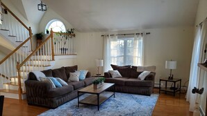 Ein geräumiges Wohnzimmer mit einer Holztreppe, zwei braunen Sofas, einem Couchtisch und einem großen Fenster mit Vorhängen.