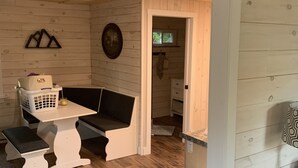 L’intérieur d’un chalet accueillant, avec un plancher en bois, un banc blanc, une petite table sur laquelle se trouve un panier, et un tableau encadré accroché au mur.