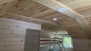Une pièce aux murs et au plafond en bois, avec des lits superposés et une fenêtre donnant sur un paysage verdoyant.