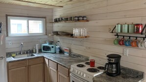 Une cuisine avec des meubles de rangement en bois, une cuisinière, un four à micro-ondes et divers ustensiles de cuisine rangés sur des étagères.