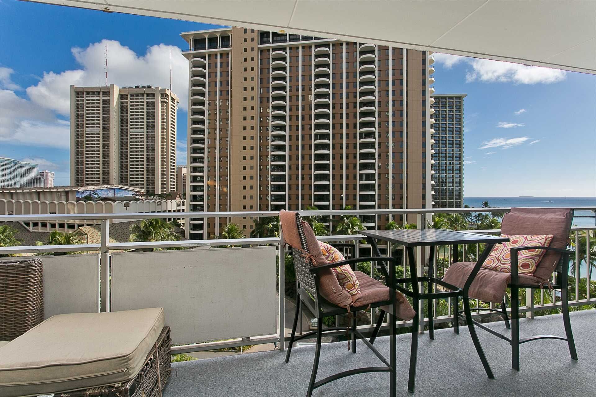 Ein Balkon mit zwei Stühlen und einem Tisch, mit Blick auf eine Skyline mit hohen Gebäuden.
