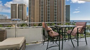 A balcony with two chairs and a table, overlooking a cityscape with tall buildings. - Ilikai 640 Ocean / Lagoon Views / Queen Bed, Sofa Bed (Waikiki)