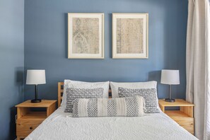 A bedroom with a bed, two nightstands, two lamps, and two framed pictures on the wall.