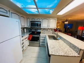 A modern kitchen with white cabinets, a built-in oven, a microwave, and a granite countertop.