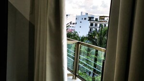 A balcony with a glass railing and a view of buildings and greenery. - Ocean Front Boutique (Playa del Carmen)