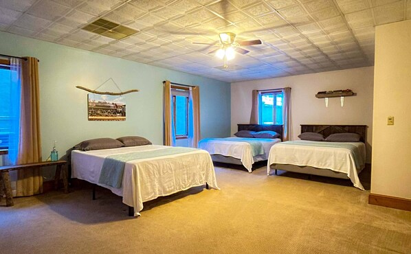 A room with three beds, a ceiling fan, and a window.