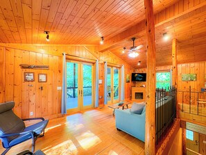 A wooden cabin interior with a sofa, a chair, a television, and a fireplace.
