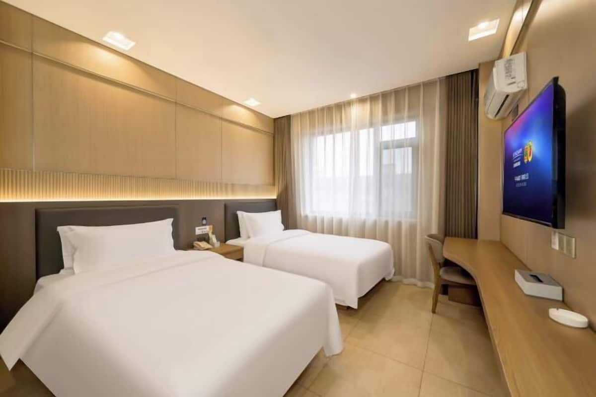 Ein Hotelzimmer mit zwei Betten, einem Fernseher, einem Schreibtisch und einem fensterbepflanzten Fenster.