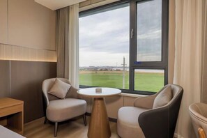 Et hotelværelse med stort vindue, to lænestole, et rundt bord og en seng.
