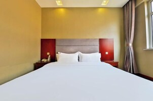 Una habitación de hotel con una cama grande, dos mesitas de noche y un ventanal con cortinas.