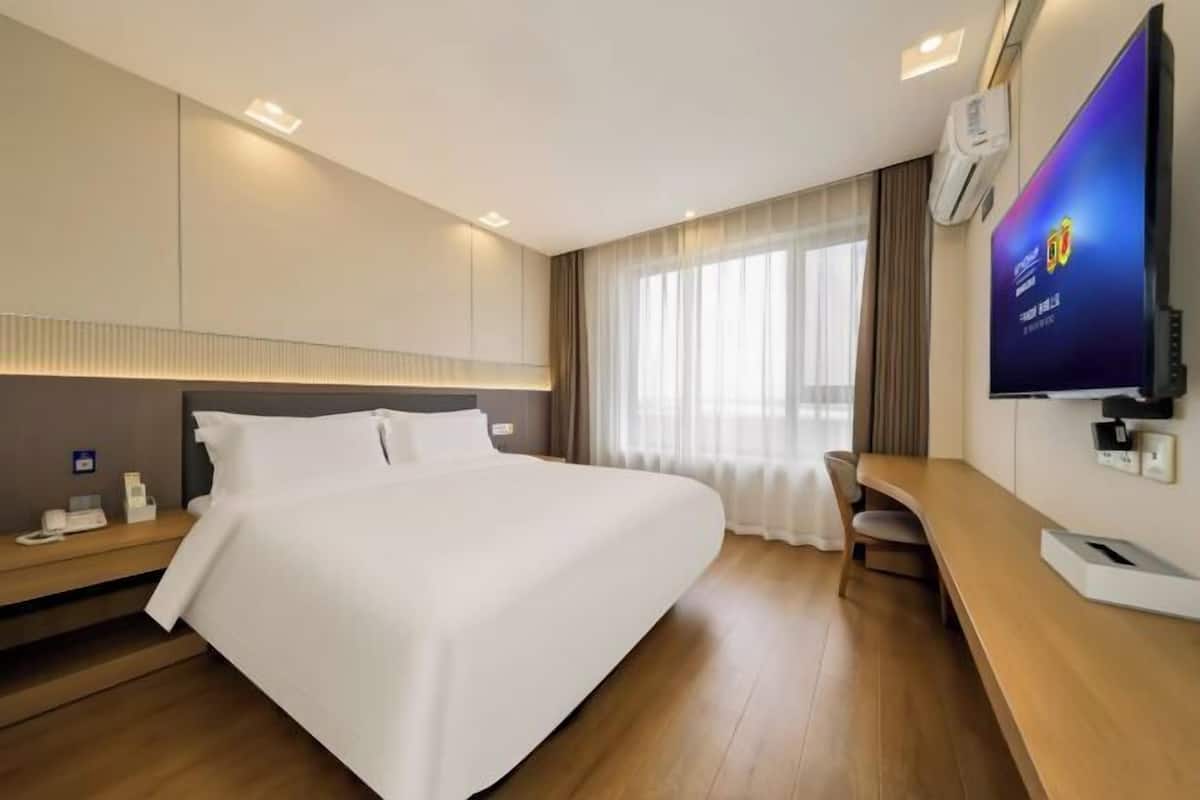 Ein Hotelzimmer mit einem großen Bett, einem Schreibtisch, einem Flachbildfernseher und einem Fenster mit Vorhängen.