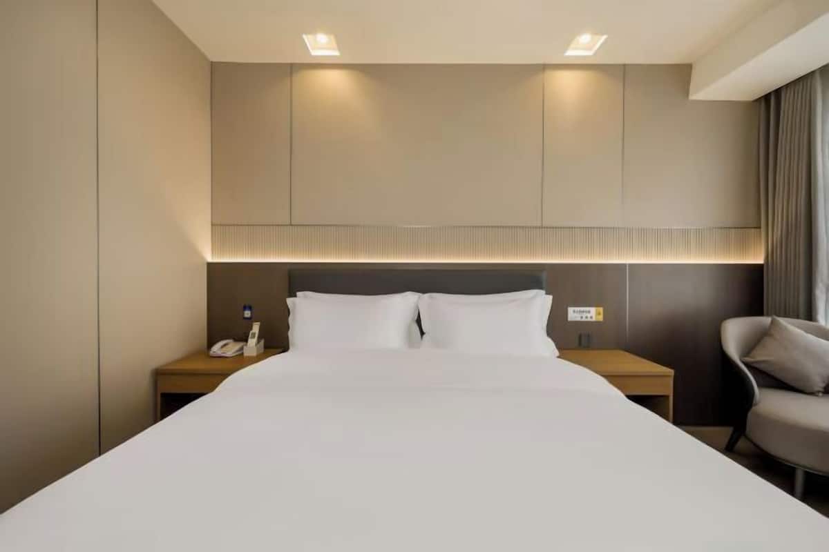 Ein Hotelzimmer mit einem großen Bett, Nachttischen, einem Sessel und einem Kopfteil mit integrierter Beleuchtung.