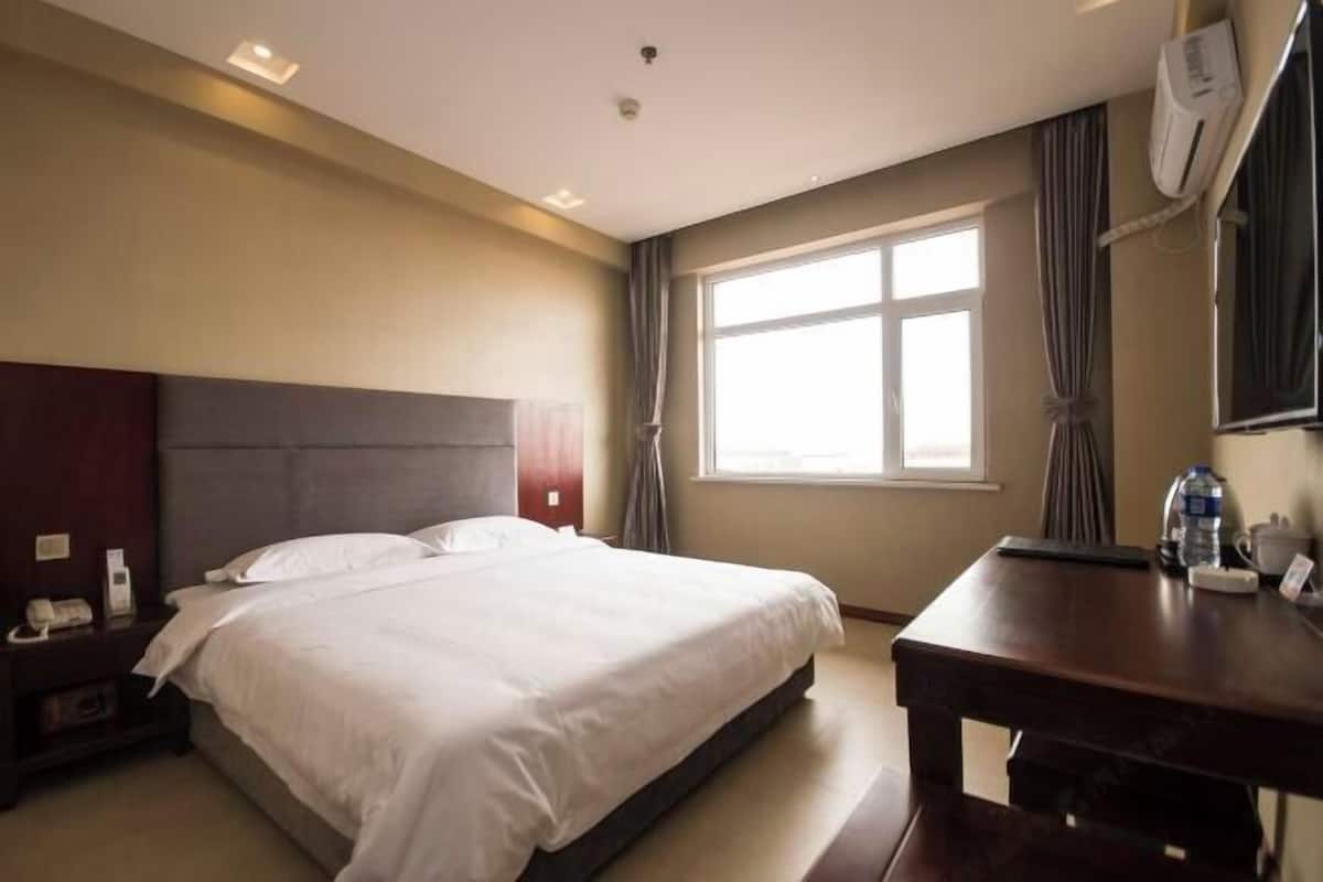 Ein Hotelzimmer mit Bett, Schreibtisch, Stuhl, einem Fenster mit Vorhängen und einer Wand-Klimaanlage.