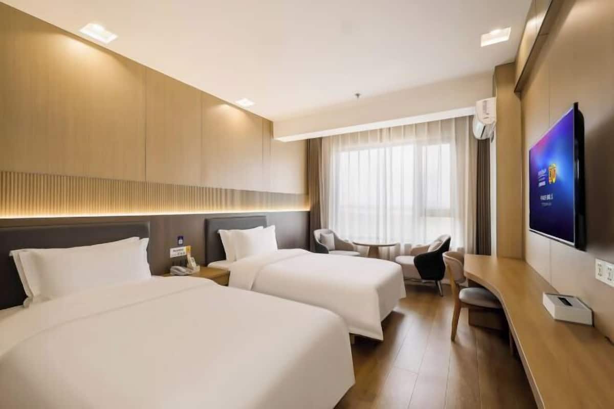 Ein Hotelzimmer mit zwei Betten, einem Schreibtisch, einem Stuhl, einem Fernseher und einem fenster mit Vorhängen.