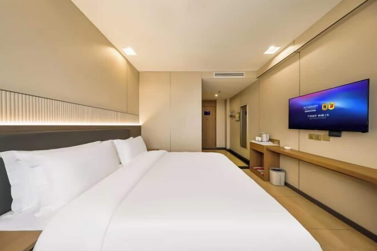 Ein Hotelzimmer mit einem großen Bett, einem an der Wand montierten Fernseher und einem Nachttisch aus Holz.