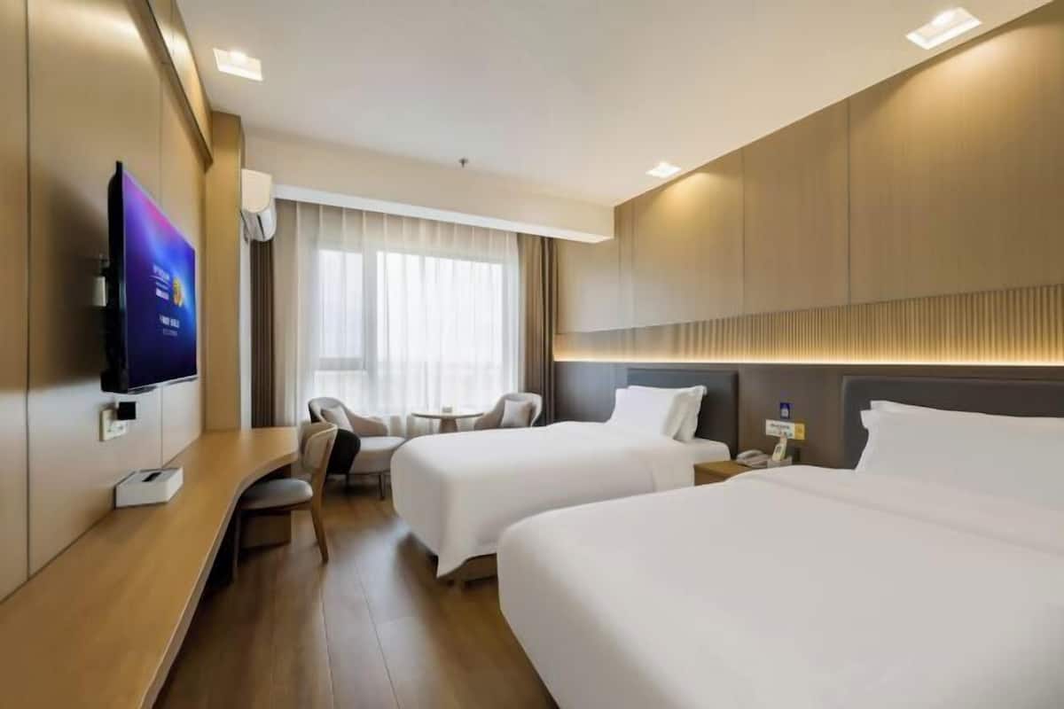 Ein Hotelzimmer mit zwei Betten, einem Fernseher, einem Schreibtisch und einem fensterbepflanzten Fenster.