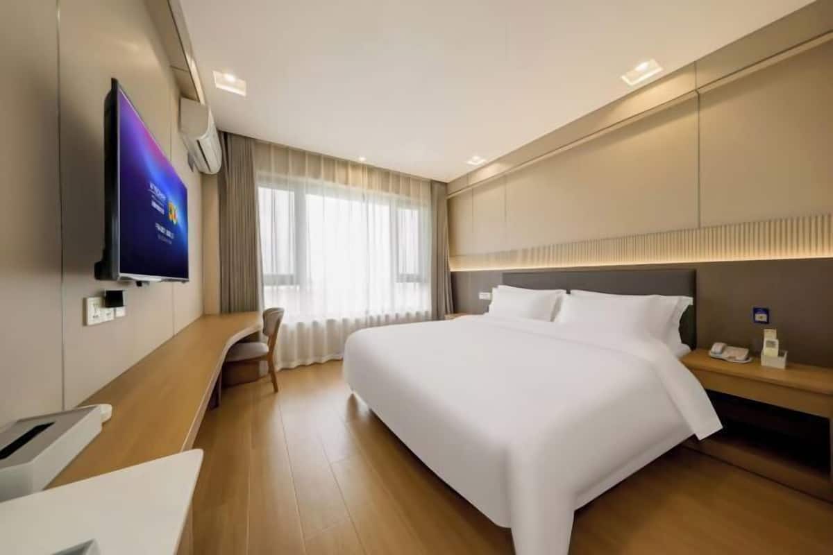 Ein Hotelzimmer mit einem großen Bett, einem Schreibtisch, einem Fernseher und einem Fenster mit Vorhängen.