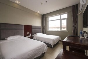 Une chambre d’hôtel avec deux lits, un bureau, une chaise, une fenêtre avec des rideaux et un climatiseur fixé au mur.