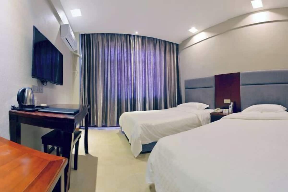 Ein Hotelzimmer mit zwei Betten, einem Schreibtisch, einem Sessel, einem Fernseher und einem Vorhang.