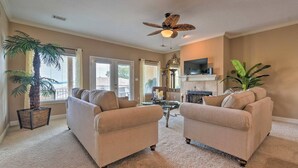 A spacious living room with two beige sofas, a ceiling fan, a fireplace, and large windows. - Lakeview Condo w/ Balcony+Pool Access, Sunrise View! (Lake Hamilton)