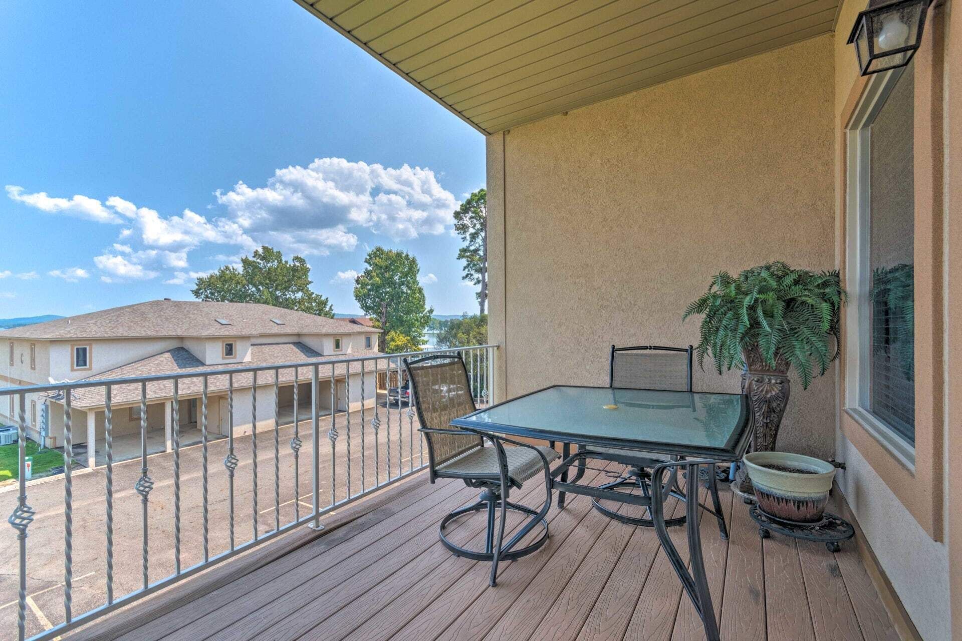 A balcony with a glass table and chairs, a potted plant, and a view of houses in the background.