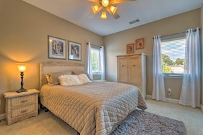 A bedroom with a bed, bedside table, lamp, ceiling fan, window with curtains, and a cabinet.