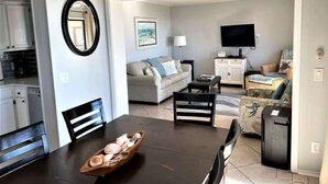 A modern living room with a dining table, sofa, and TV. - Oceanfront 3rd Floor Villa at Admiral's Row - Stunning Beach Views (Hilton Head Island)