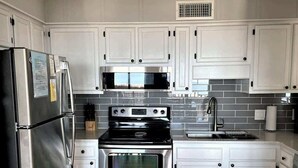 A modern kitchen with white cabinets, stainless steel appliances, a microwave, a stove, and a sink. - Oceanfront 3rd Floor Villa at Admiral's Row - Stunning Beach Views (Hilton Head Island)