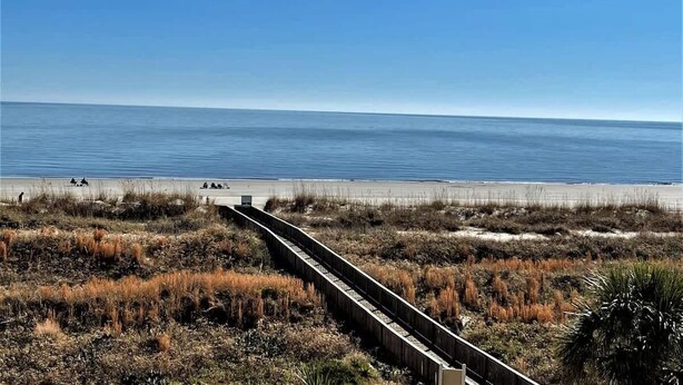 A coastal view with a sandy beach and a wooden boardwalk leading to the water. - Oceanfront 3rd Floor Villa at Admiral's Row - Stunning Beach Views (Hilton Head Island)