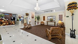 A hotel lobby with a reception desk, wicker chairs, a chandelier, and a patterned carpet.