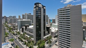A cityscape with modern high-rise buildings, a clear sky, and palm trees lining the streets. - Royal Kuhio 1708 - Spacious Corner Unit w/ Ocean City Views in Heart of Waikiki (Waikiki)