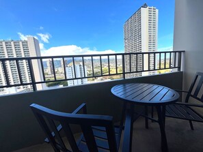 Un balcon avec une table ronde et deux chaises, donnant sur un paysage urbain composé d’immeubles de grande hauteur et d’une rivière.