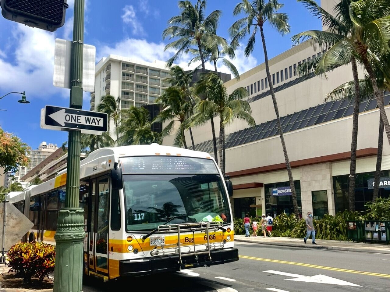 A bus with a "ONE WAY" sign, a building with a "MONSTER" sign, and palm trees.
